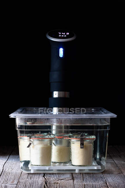 Cheesecake in glass tubs preparing in chief cooking sous-vide placed on wooden table on black background — Stock Photo