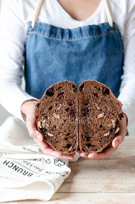 Руки женщины в фартуке держат ржаной хлеб с изюмом и орехами — стоковое фото