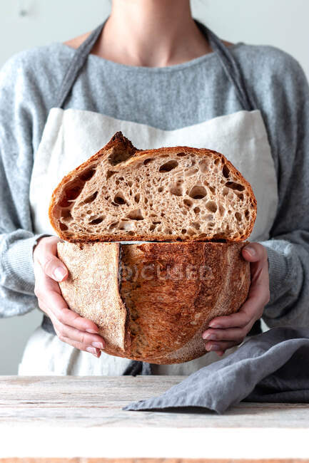 Hands of woman in kitchen apron holding both hands cutting homemade bread — Stock Photo