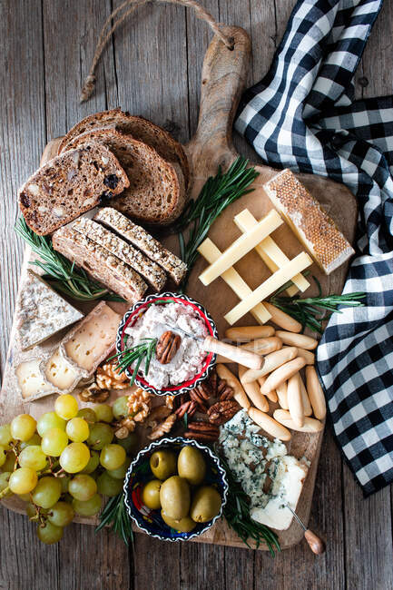 De la composition ci-dessus de pain de seigle frais, fromage, grappe de raisin et olives placés sur une planche de bois — Photo de stock