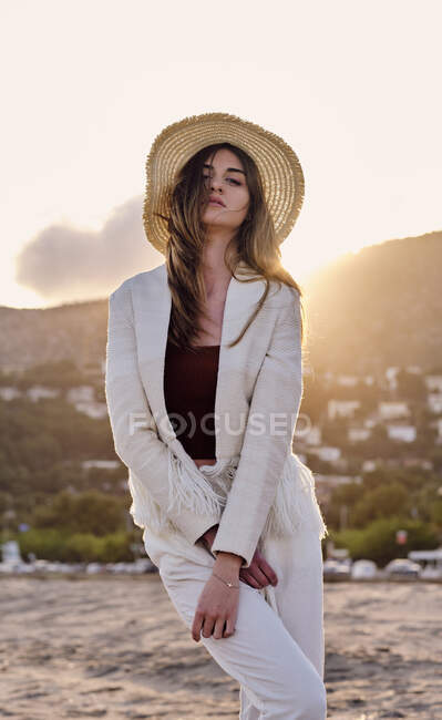 Un modello di moda capelli lunghi con un cappello in spiaggia al tramonto in una giornata estiva — Foto stock