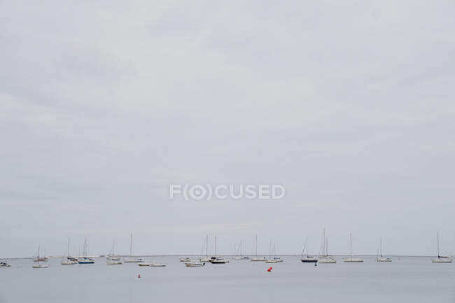Muitos barcos à vela flutuando na água do mar calma contra o céu nublado cinza no dia maçante no porto — Fotografia de Stock