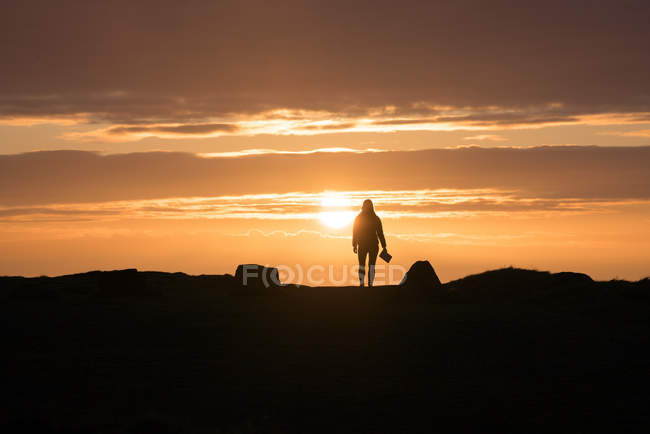 Silhouette femminile con libro in piedi al tramonto in controluce in terreno roccioso in Galles — Foto stock