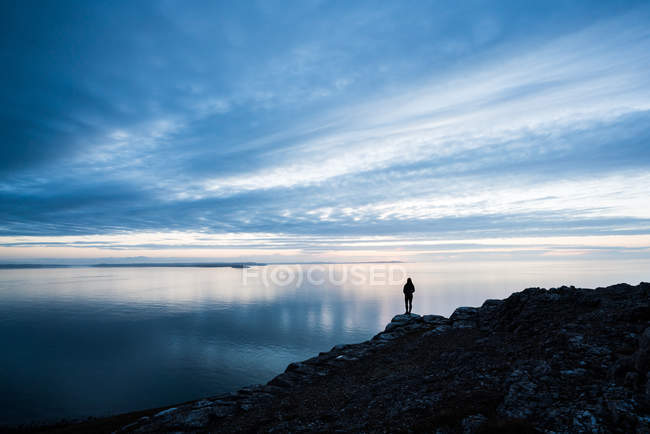 Silhouette di donna in piedi sulla costa rocciosa al tramonto in Galles — Foto stock