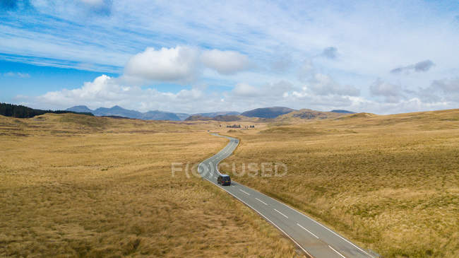 Автомобиль едет по одинокой асфальтовой дороге в горной местности в солнечный день в Уэльсе — стоковое фото
