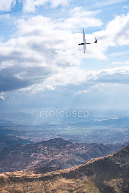 Small glider plane flying over rocky mountains in cloudy sky in summer sunny day in Wales — Stock Photo