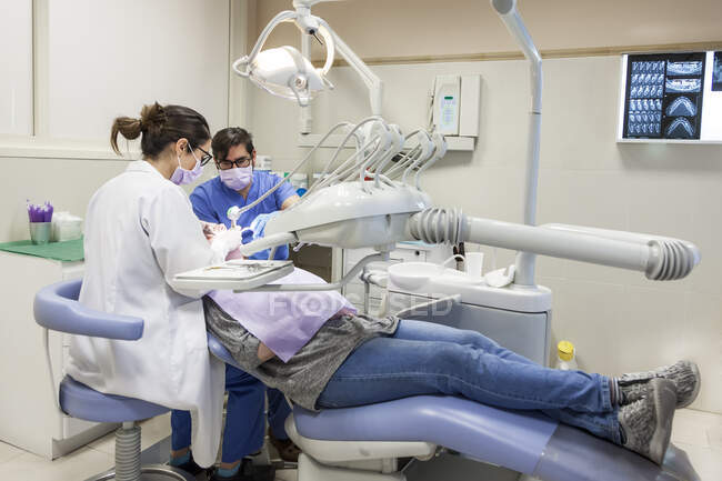 Dentista femenina que atiende a la paciente con su asistente - foto de stock