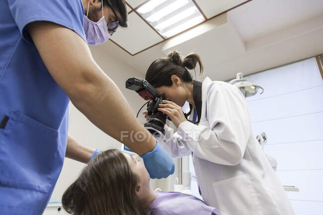 Desde abajo estomatólogo tomar fotos de la boca del paciente joven con cámara en odontología - foto de stock