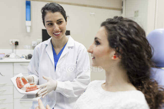 Женщина-стоматолог учит пациента лечению ее зубного протеза — стоковое фото