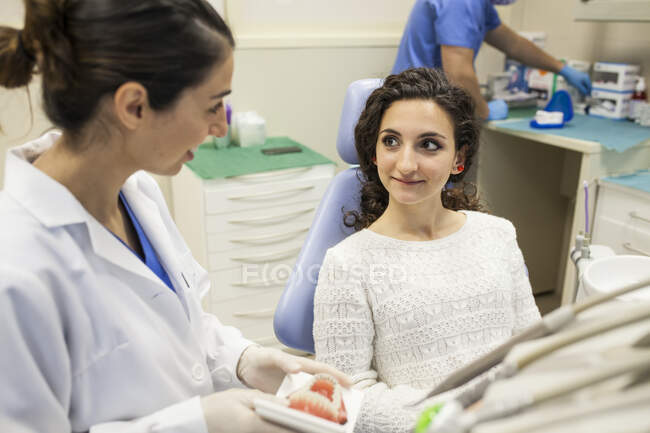 Dentista mujer enseñando a la paciente el tratamiento para su prótesis dental - foto de stock