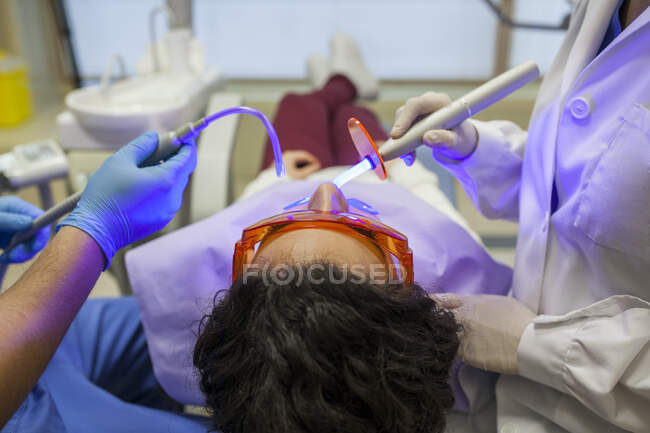 Dentista y su asistente usando la lámpara ultravioleta en la dentadura postiza del paciente - foto de stock