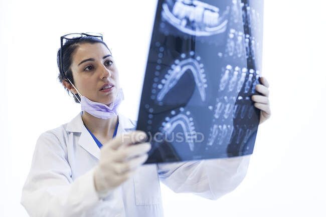 Jeune belle dentiste femme en robe médicale, gants, masque et lunettes de contrôle x-ray isolé sur fond blanc — Photo de stock