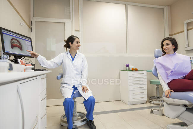 Female dentist advising the patient and showing her treatment — Stock Photo