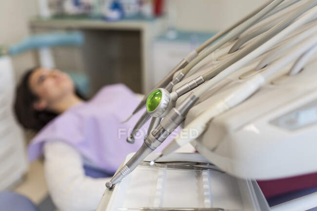 Zahnarzt zeitgenössische Werkzeuge wie Bohrer, Scharfer, Schaber und Schnitzer mit junger Patientin im Hintergrund in Zahnklinik — Stockfoto