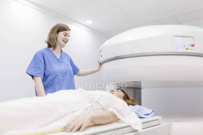 Mujer de mediana edad y su médico en una máquina de resonancia magnética abierta esperando a que comience la prueba - foto de stock