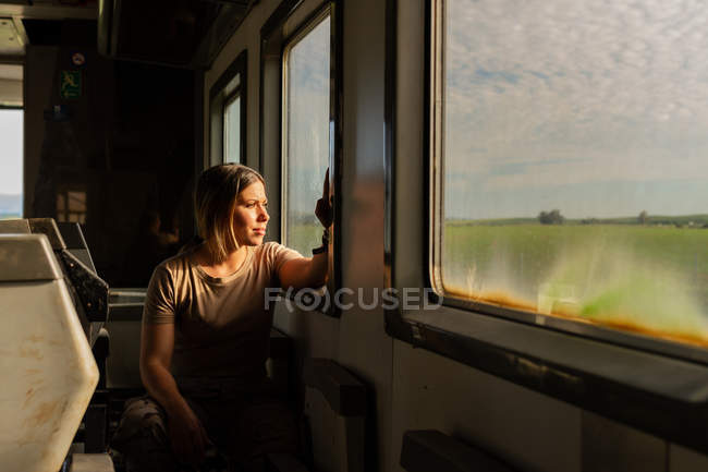 Mujer soldado mirando por la ventana mientras viaja por el campo en vehículo militar - foto de stock