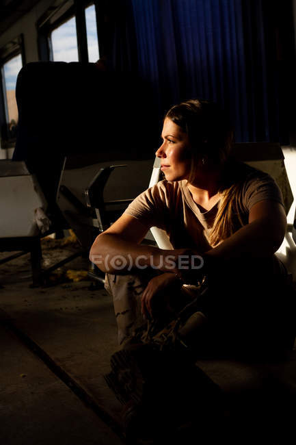 Serious military woman in uniform looking away while sitting on floor of army transport — Stock Photo