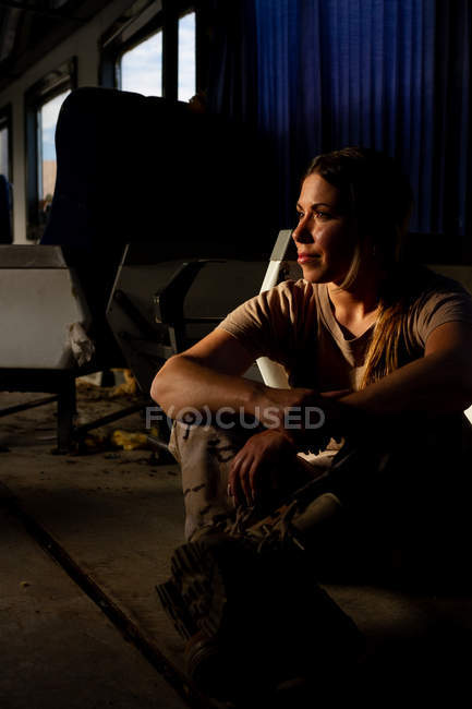 Mujer militar seria en uniforme mirando hacia otro lado mientras está sentada en el suelo del transporte del ejército - foto de stock