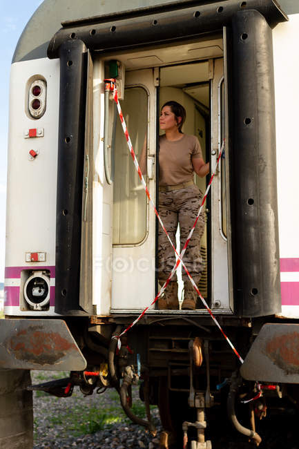 Starke Soldatin, die wegschaut und denkt, während sie in der Tür eines grunzigen Militärfahrzeugs auf dem Land steht — Stockfoto