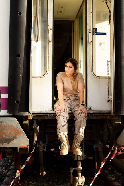 Starke Soldatin, die wegschaut und denkt, während sie in der Tür eines grunzigen Militärfahrzeugs auf dem Land sitzt — Stockfoto
