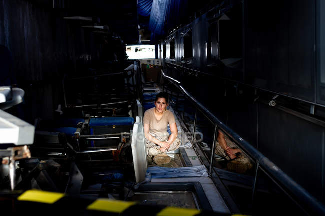 Attractive female soldier looking at camera while sitting inside dark hangar — Stock Photo