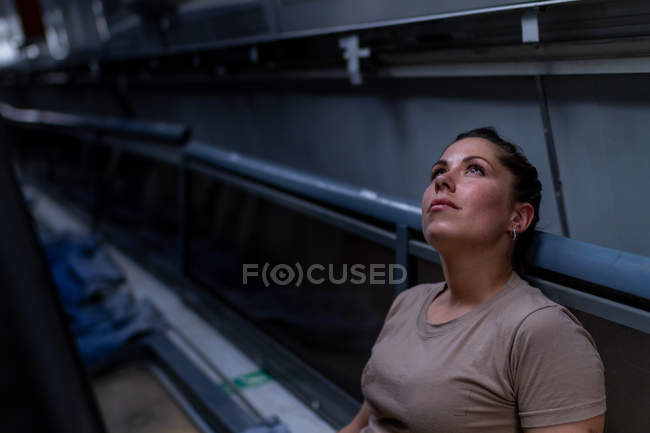 Atractiva soldado mujer mirando hacia arriba mientras está sentada dentro del moderno transporte militar - foto de stock