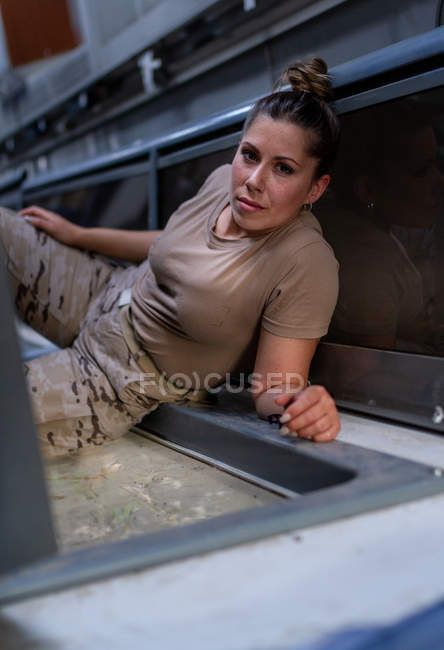 Жінка-солдат дивиться на камеру, лежачи на підлозі сучасного військового транспорту — стокове фото