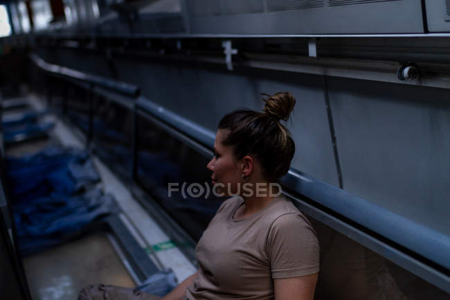 Mujer militar seria en uniforme mirando hacia otro lado mientras está sentada en el suelo del transporte del ejército - foto de stock