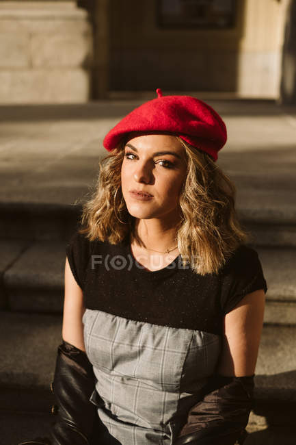 Porträt einer jungen Frau mit trendiger roter Baskenmütze, die an sonnigen Tagen in die Kamera blickt — Stockfoto