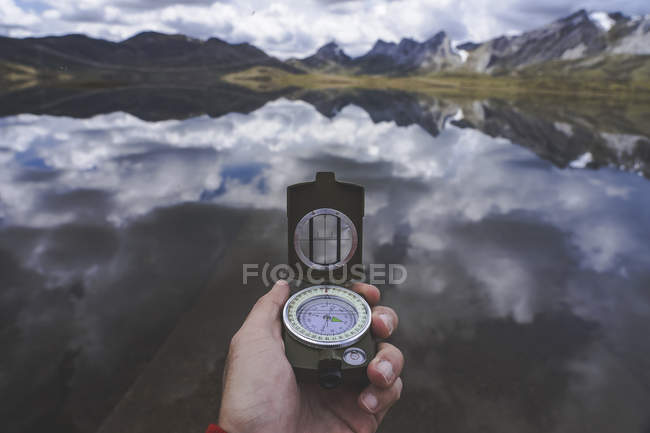 Hand of anonymous traveler holding compass against tranquil mountain lake on cloudy day in Spanish countryside — Stock Photo