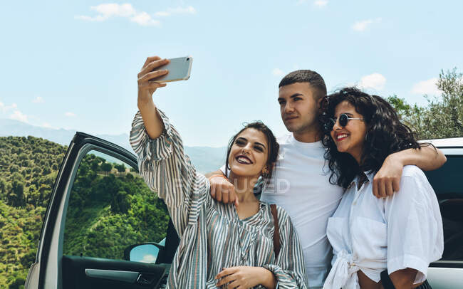 Grupo de amigos disfrutando de una conversación fuera del coche. Hablan y selfies en un lugar turístico - foto de stock