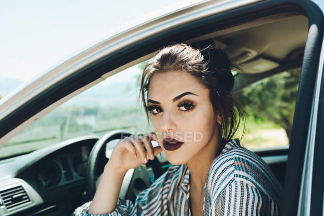 Retrato de una chica bonita sentada en la silla del coche mientras recibe los rayos del sol en su cara - foto de stock