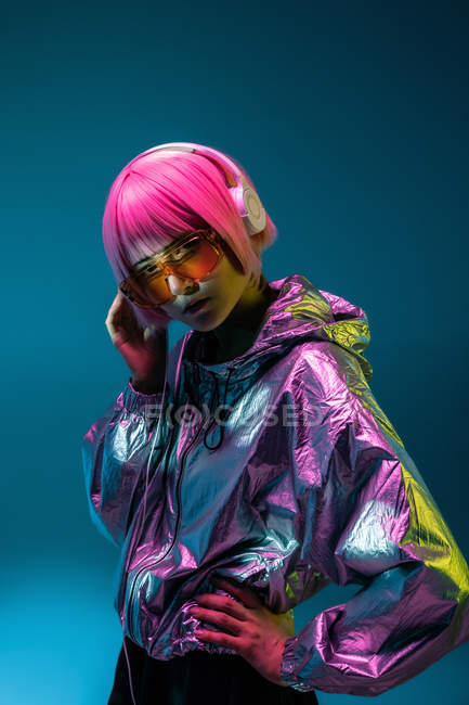 Young Asian woman with stylish pink haircut and sparkly silver jacket standing and listening music — Stock Photo