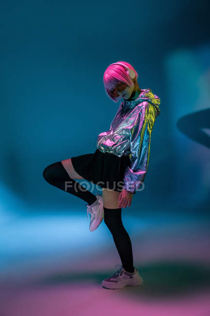 Young Asian woman with stylish pink haircut and sparkly silver jacket standing on one leg and listening music — Stock Photo