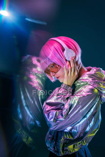 Alla moda attraente giovane donna asiatica con i capelli rosa in giacca d'argento ascoltare musica su sfondo scuro con riflessione — Foto stock