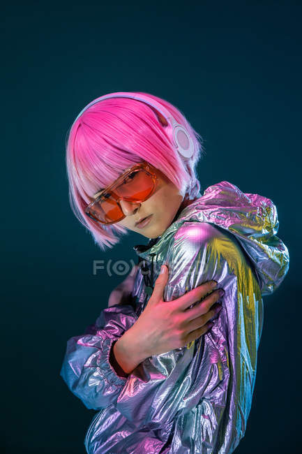 Junge Asiatin mit stylischem rosa Haarschnitt und funkelnder silberner Jacke stehend und Musik hörend — Stockfoto