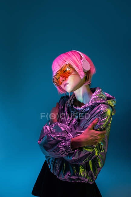 Jeune femme asiatique avec coupe de cheveux rose élégant et veste en argent brillant debout et écouter de la musique — Photo de stock