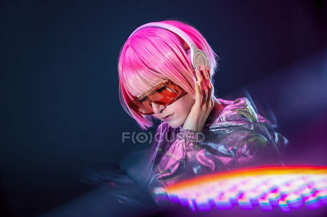 Stylische junge Asiatin mit rosafarbenen Haaren und silberner Jacke, die mit geschlossenen Augen Musik hört — Stockfoto