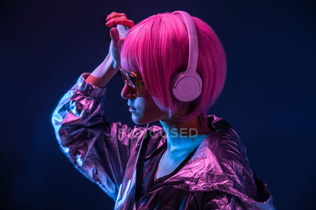 Trendy Japanese young pretty woman in red sunglasses and headphones posing on dark background — Stock Photo