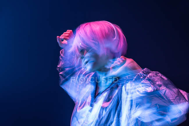 Jovem mulher asiática subcultural com cabelo rosa disperso e jaqueta de prata dançando enquanto ouve música em fones de ouvido — Fotografia de Stock