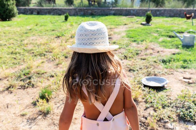 Niña en vestido y sombrero ayudando en el jardín en el día soleado en la granja - foto de stock