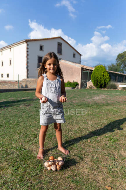 Маленькая девочка держит яйца на ферме и смотрит в камеру — стоковое фото