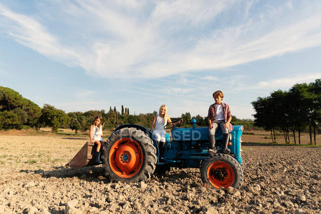 Group of young friends siting and looking at camera on a blue tractor in a rural terrain — Stock Photo