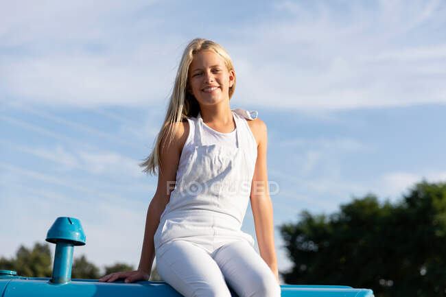 Petite fille assise sur un tracteur contre un ciel nuageux à la ferme — Photo de stock