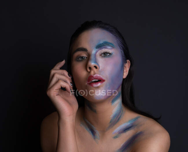 Jeune femme attrayante avec peinture visage de couleur bleu et argent sur fond noir regardant la caméra — Photo de stock