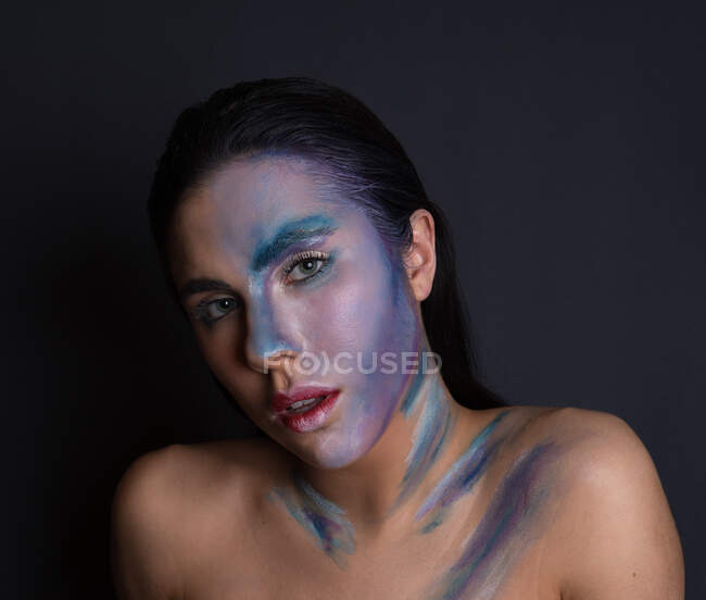 Jovem mulher atraente com pintura azul e cor de prata rosto no fundo preto olhando para a câmera — Fotografia de Stock