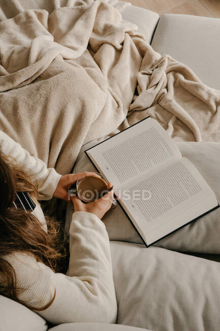 Невпізнана жінка сидить на ліжку читає книгу і п'є каву — стокове фото