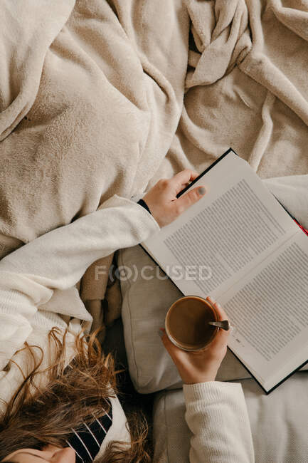 Unrecognizable woman sitting on the bed reading a book and drinking coffee — Stock Photo