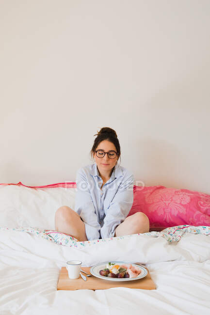 Retrato de mulher com olhos fechados enquanto se senta na cama em frente a uma bandeja com comida saudável — Fotografia de Stock