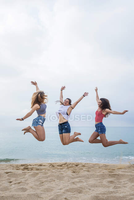 Vista frontale di un gruppo di tre giovani amiche sorridenti che saltano e si divertono sulla spiaggia — Foto stock